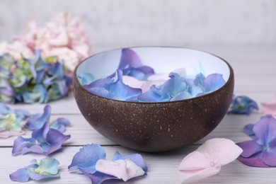 Photo of Spa composition. Aromatic water in bowl and flowers on white wooden table, closeup