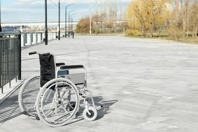 Photo of Empty wheelchair on embankment on sunny day. Space for text