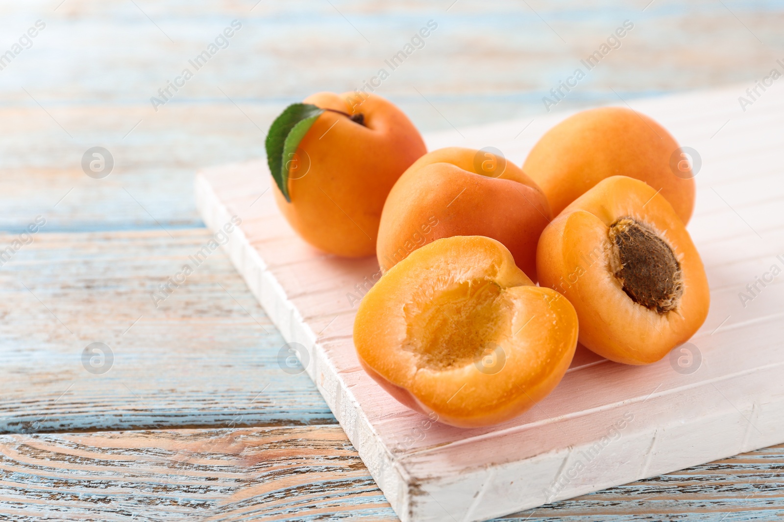 Photo of Board with delicious apricots on light wooden background, closeup. Space for text