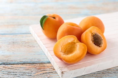 Board with delicious apricots on light wooden background, closeup. Space for text