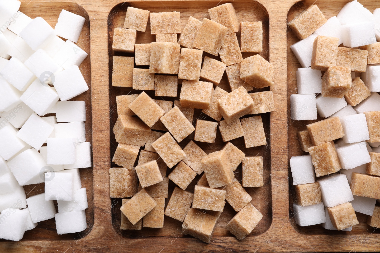 Photo of Wooden tray with brown and white sugar cubes, top view