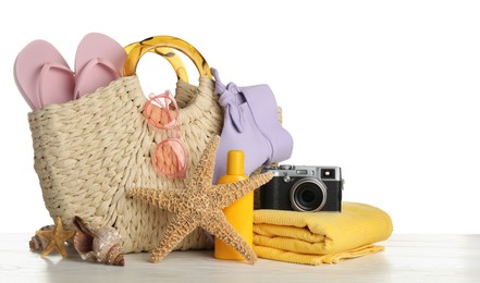 Photo of Bag with different beach objects on wooden table against white background