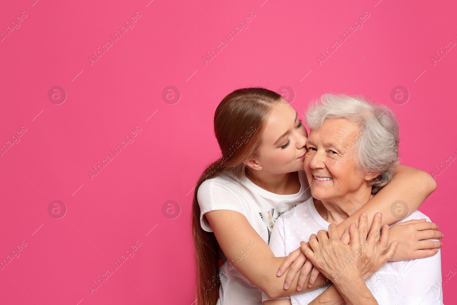 Photo of Young woman kissing her grandmother on pink background. Space for text