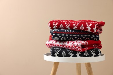 Photo of Stack of different Christmas sweaters on white table against beige background. Space for text