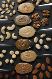 Tasty nut butters in spoons and raw nuts on dark gray table, flat lay