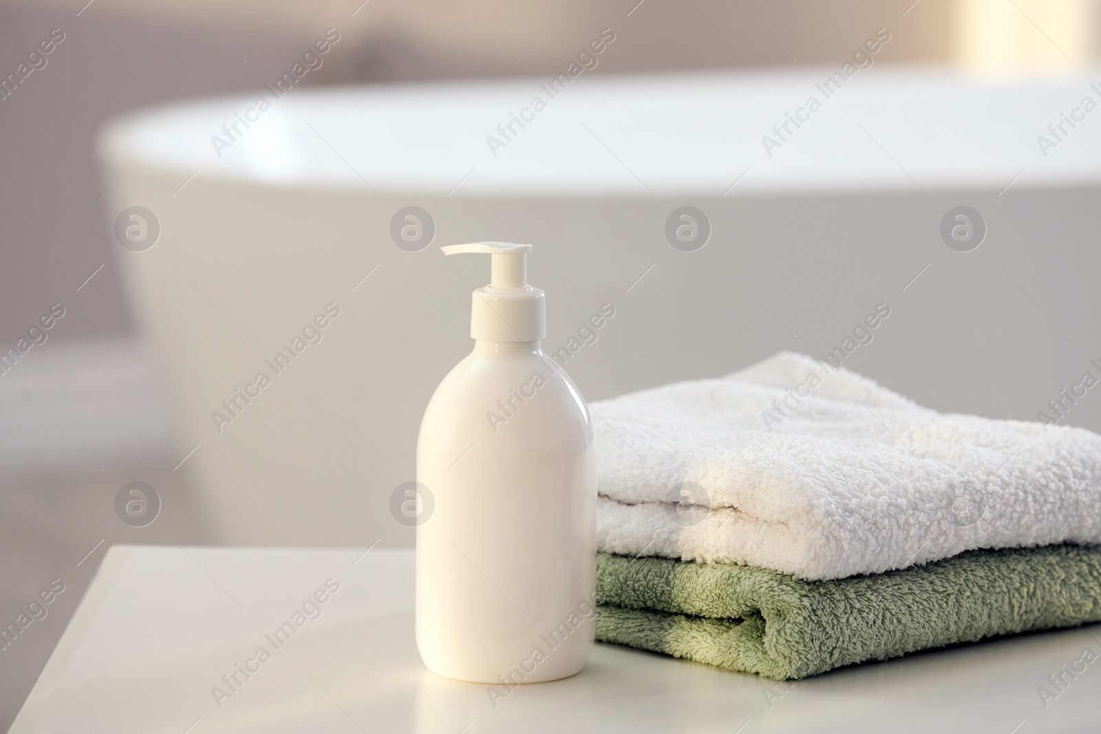 Photo of Bottle of bubble bath and towels on white table in bathroom, space for text