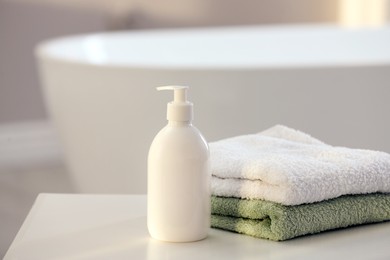 Photo of Bottle of bubble bath and towels on white table in bathroom, space for text