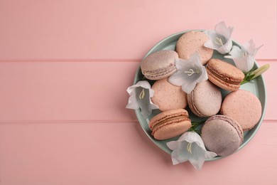 Photo of Delicious macarons and flowers on pink wooden table, top view. Space for text