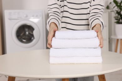 Woman with stack of folded towels at white table in laundry room, closeup. Space for text