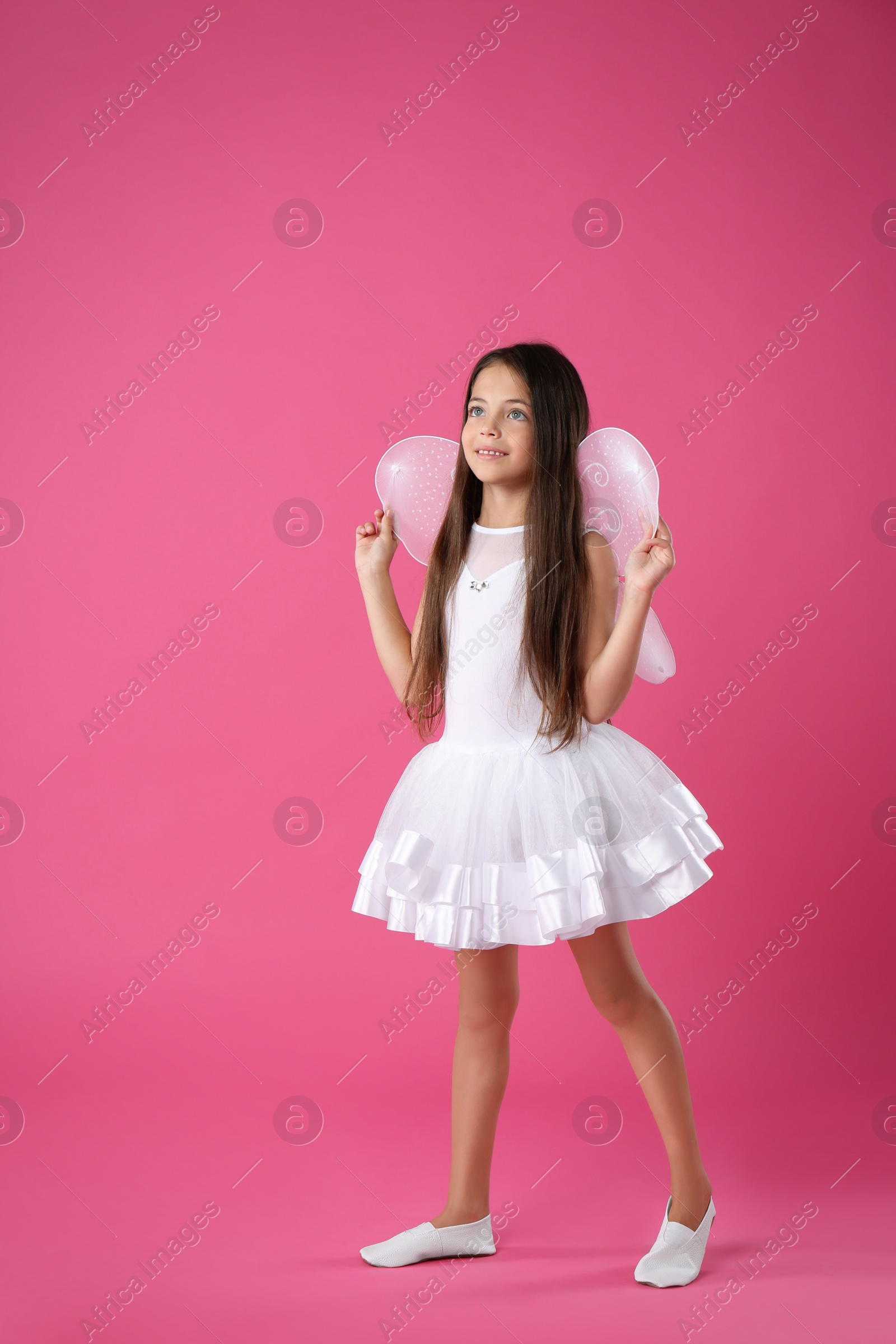 Photo of Cute little girl in fairy costume with white wings on pink background