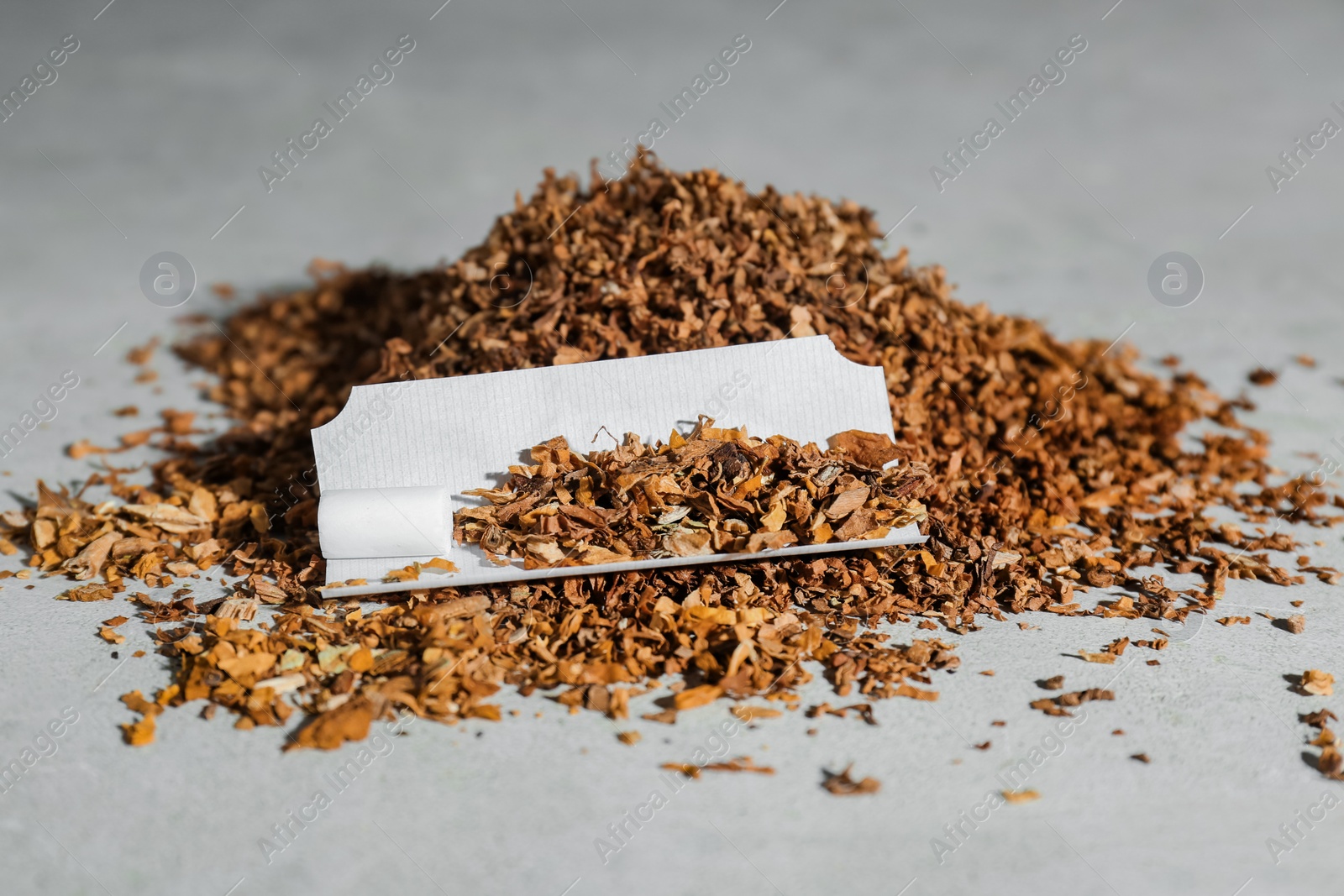 Photo of Paper and tobacco on light grey table. Making hand rolled cigarette