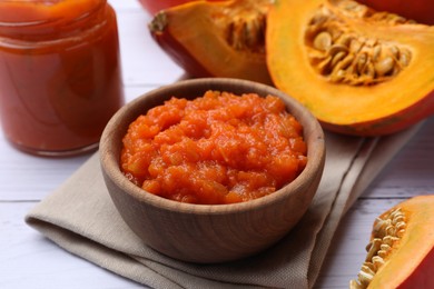 Photo of Delicious pumpkin jam and fresh pumpkin on white wooden table, closeup