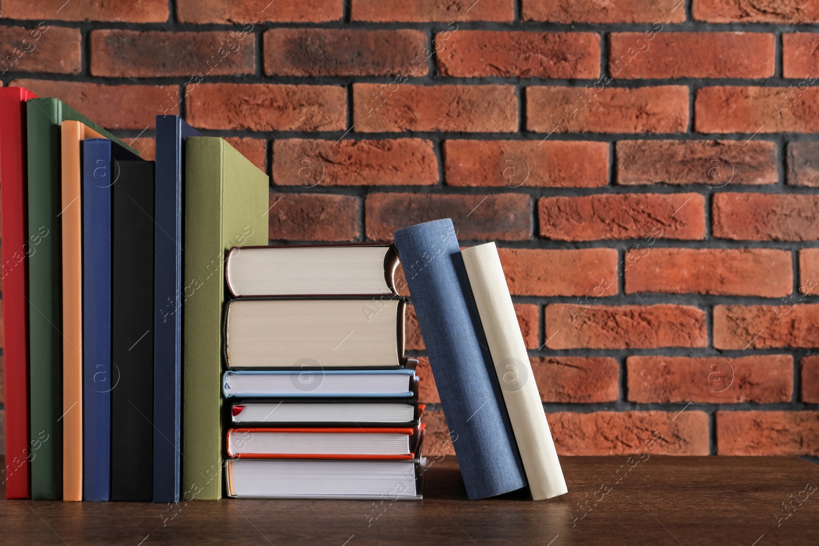 Photo of Many hardcover books on wooden table near brick wall. Space for text