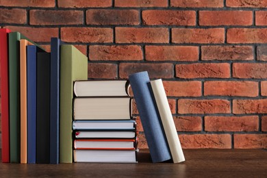 Many hardcover books on wooden table near brick wall. Space for text