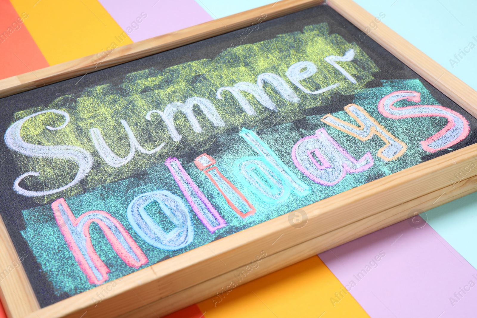 Photo of Chalkboard with phrase SUMMER HOLIDAYS on color background, closeup. School's out