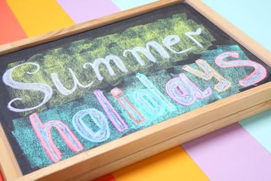 Chalkboard with phrase SUMMER HOLIDAYS on color background, closeup. School's out