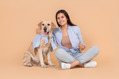 Happy woman with cute Labrador Retriever on beige background