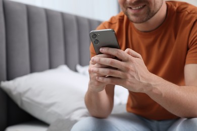 Photo of Man sending message via smartphone on bed at home, closeup. Space for text