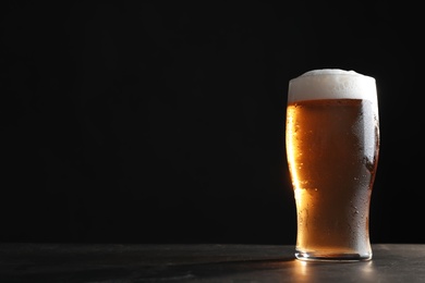 Photo of Cold tasty beer on grey table against dark background. Space for text