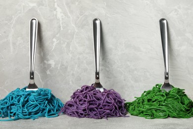 Spaghetti painted with different food colorings and forks on light grey table