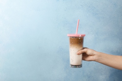 Woman holding glass of caramel macchiato on color background, closeup. Space for text