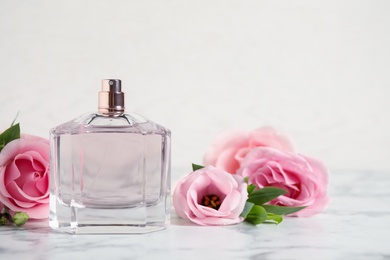 Photo of Bottle of perfume and beautiful flowers on white marble table. Space for text