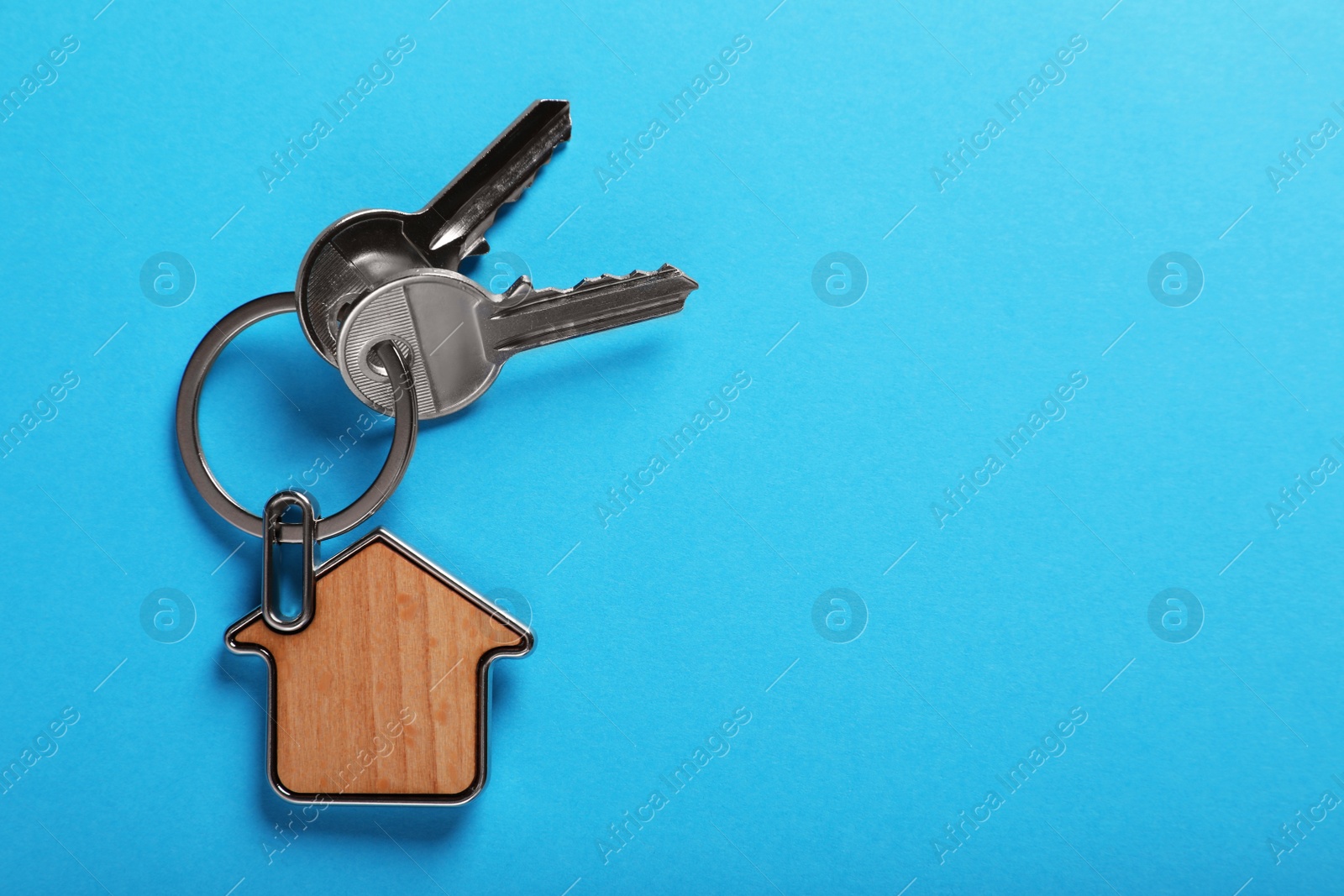 Photo of Keys with trinket in shape of house on blue background, top view and space for text. Real estate agent services