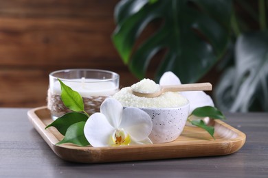 Natural sea salt in bowl, candle and beautiful orchid flower on wooden table