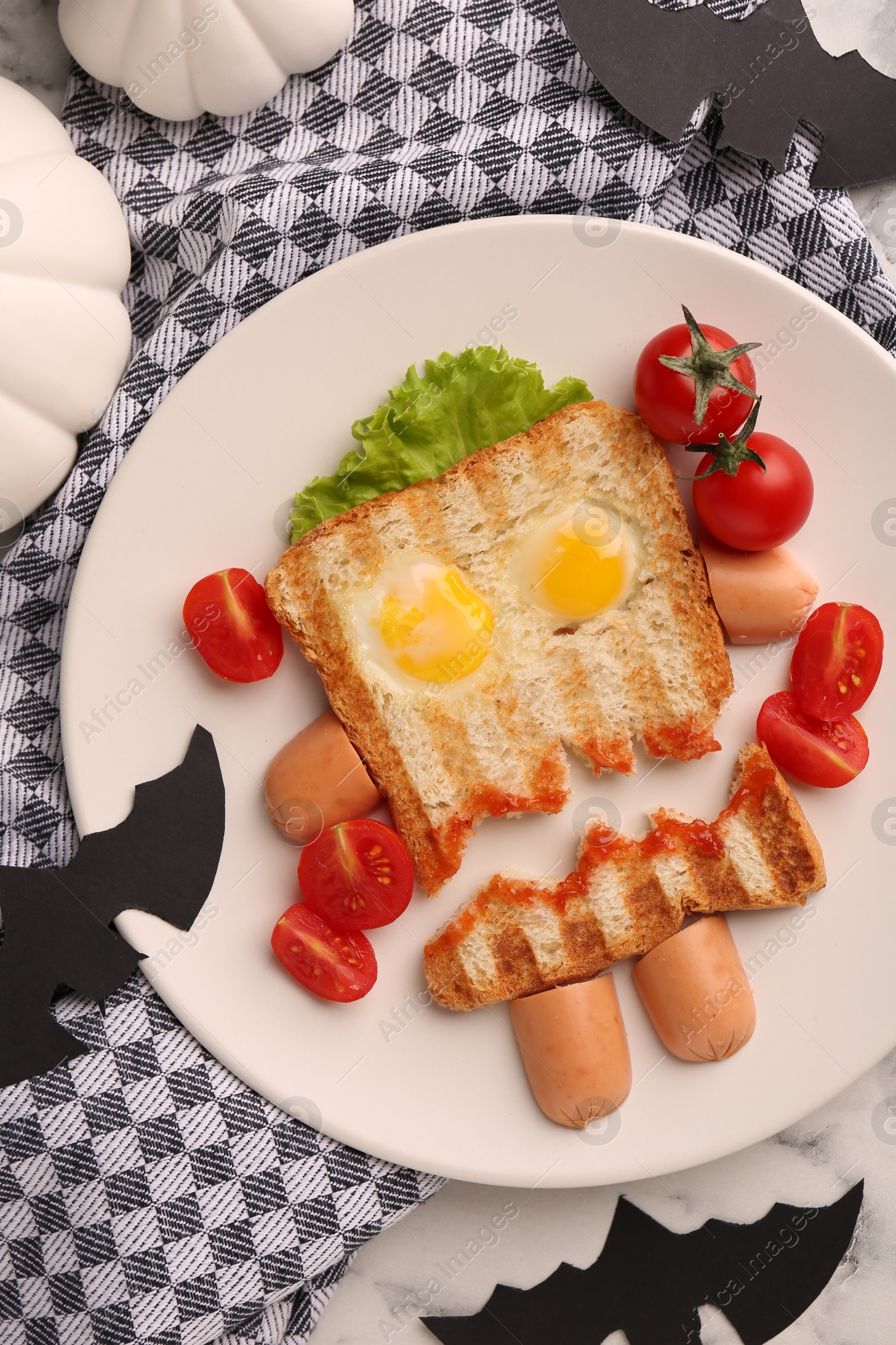 Photo of Cute monster sandwich with cherry tomatoes, fried eggs and sausages on white marble table, flat lay. Halloween snack