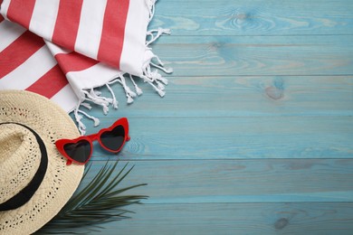 Photo of Beach towel, heart shaped sunglasses and straw hat on light blue wooden background, flat lay. Space for text