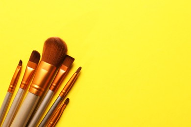 Photo of Different makeup brushes on yellow background, flat lay. Space for text