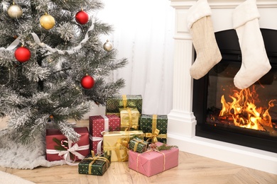 Many different gifts near Christmas tree and fireplace indoors