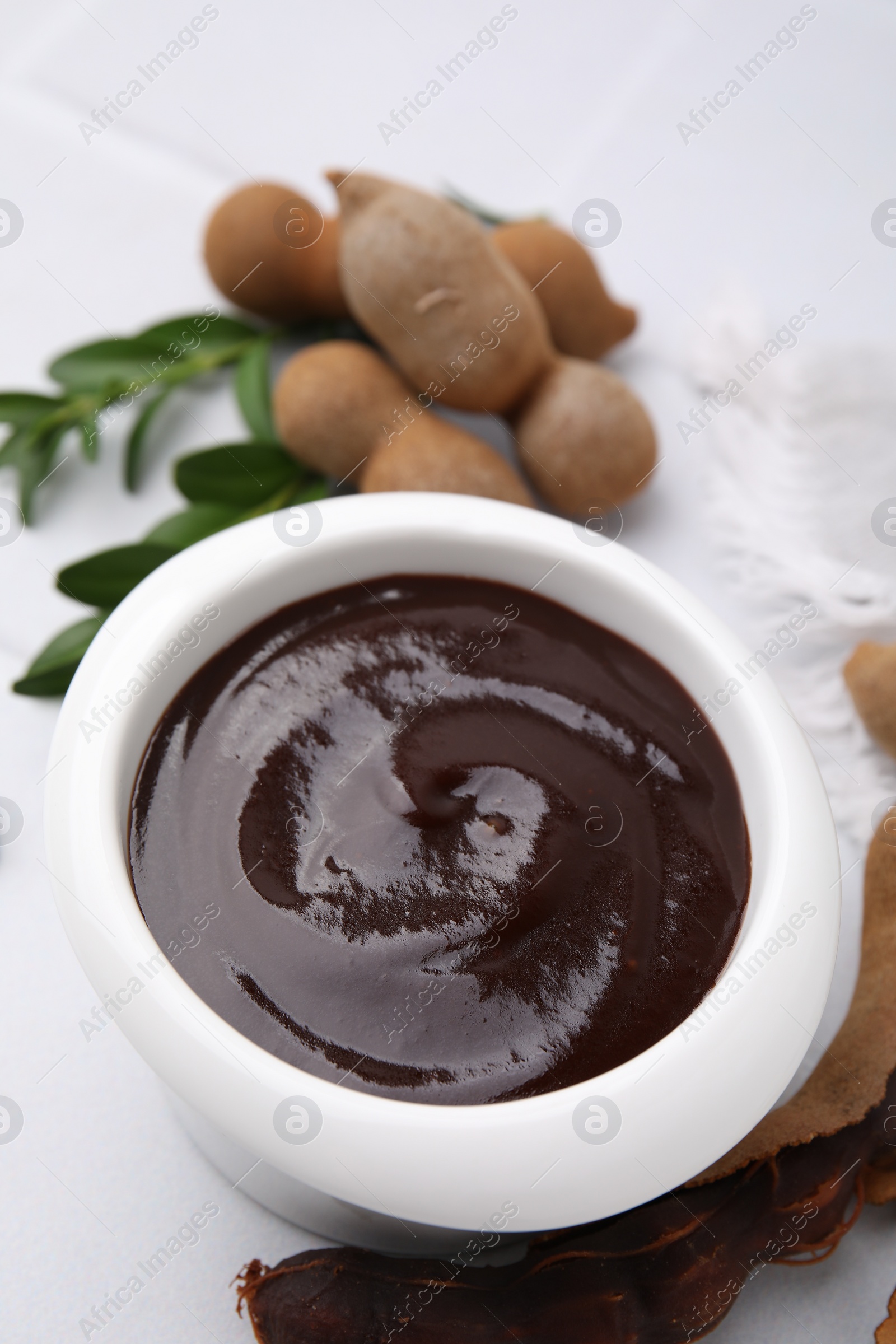 Bowl of tasty tamarind sauce and fresh pods on white table Photo of Bowl of tasty tamarind sauce and fresh pods on white table