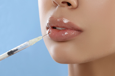 Photo of Young woman getting lips injection on light blue background, closeup