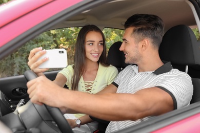 Happy young couple taking selfie in car on road trip