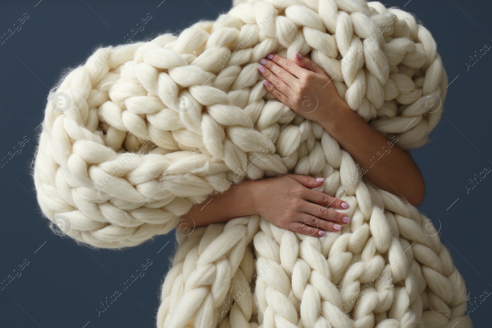 Photo of Woman holding soft knitted blanket on grey background, closeup