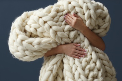 Photo of Woman holding soft knitted blanket on grey background, closeup