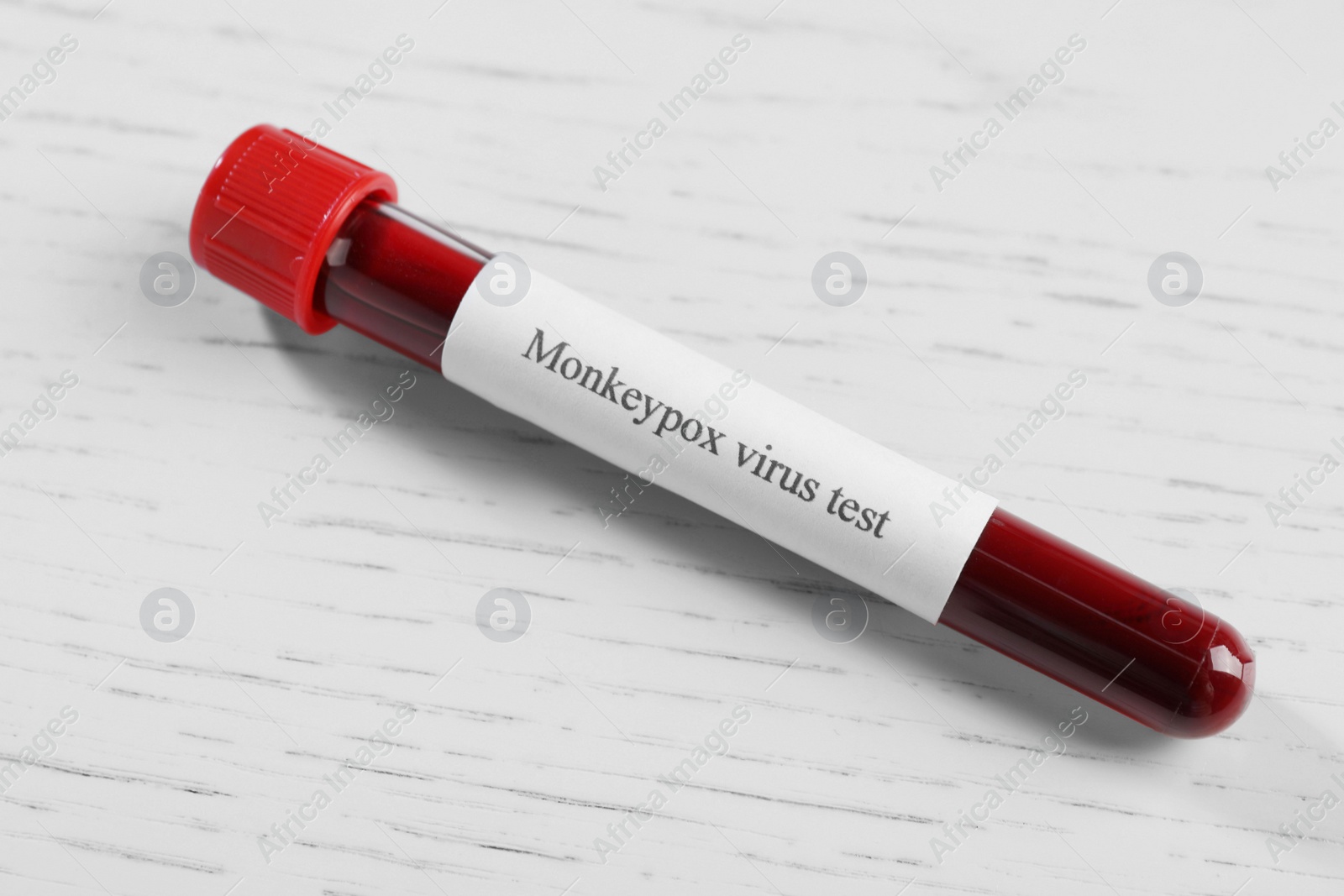 Photo of Sample tube with label Monkeypox Virus Test and blood on white wooden table