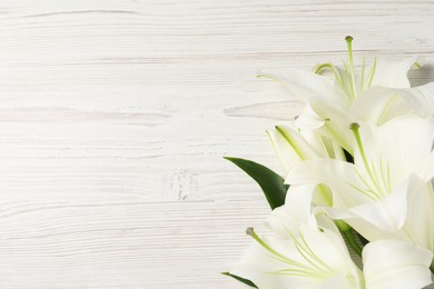 Beautiful lily flowers on white wooden table, flat lay. Space for text