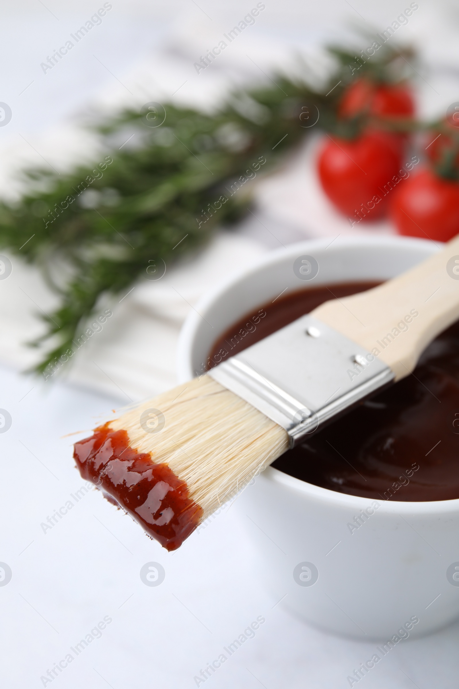 Photo of Marinade in bowl and basting brush on white table, closeup