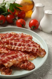 Photo of Plate with fried bacon slices, tomatoes, spices and parsley on grey textured table, closeup