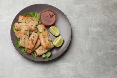 Photo of Tasty fried spring rolls with lettuce, lime and sauce on gray table, top view. Space for text