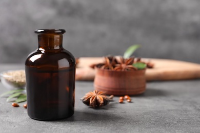 Photo of Bottle of essential oil and anise on grey table. Space for text