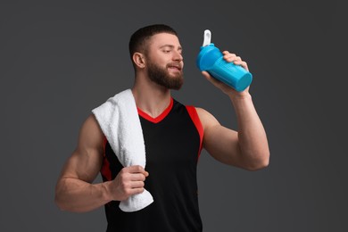 Photo of Young man with muscular body holding shaker of protein and towel on grey background