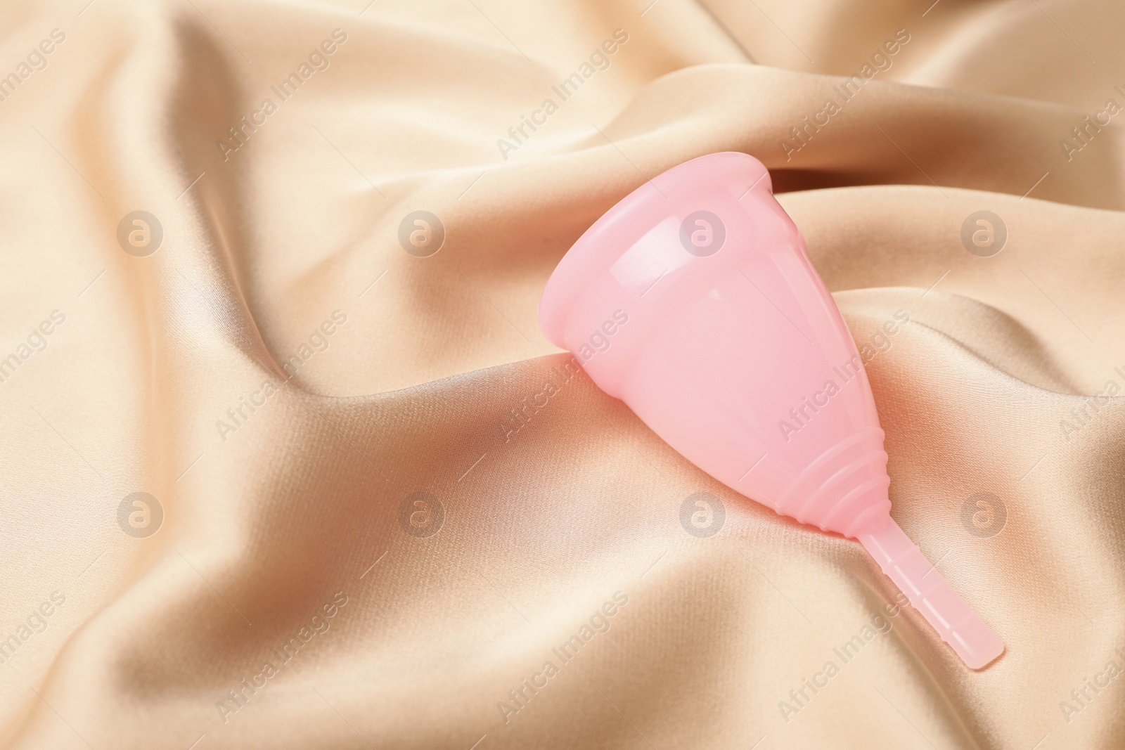 Photo of Menstrual cup on beige silk fabric. Space for text