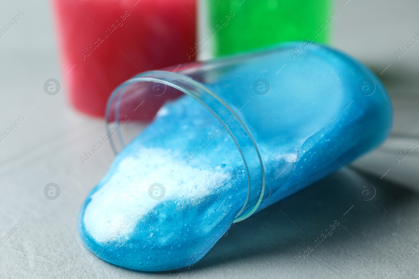 Photo of Overturned plastic container with light blue slime on grey background, closeup
