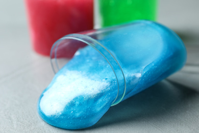 Photo of Overturned plastic container with light blue slime on grey background, closeup