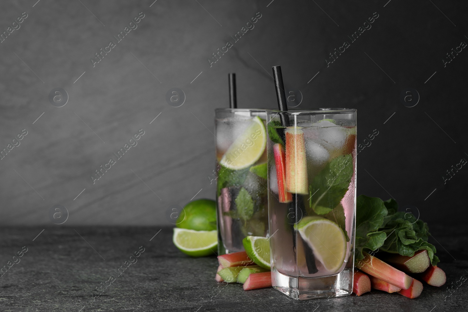 Photo of Tasty rhubarb cocktail with lime on black table, space for text