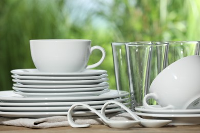 Set of clean dishware and glasses on wooden table against blurred background