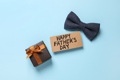 Photo of Card with phrase HAPPY FATHER'S DAY, bow tie and gift box on light blue background, flat lay